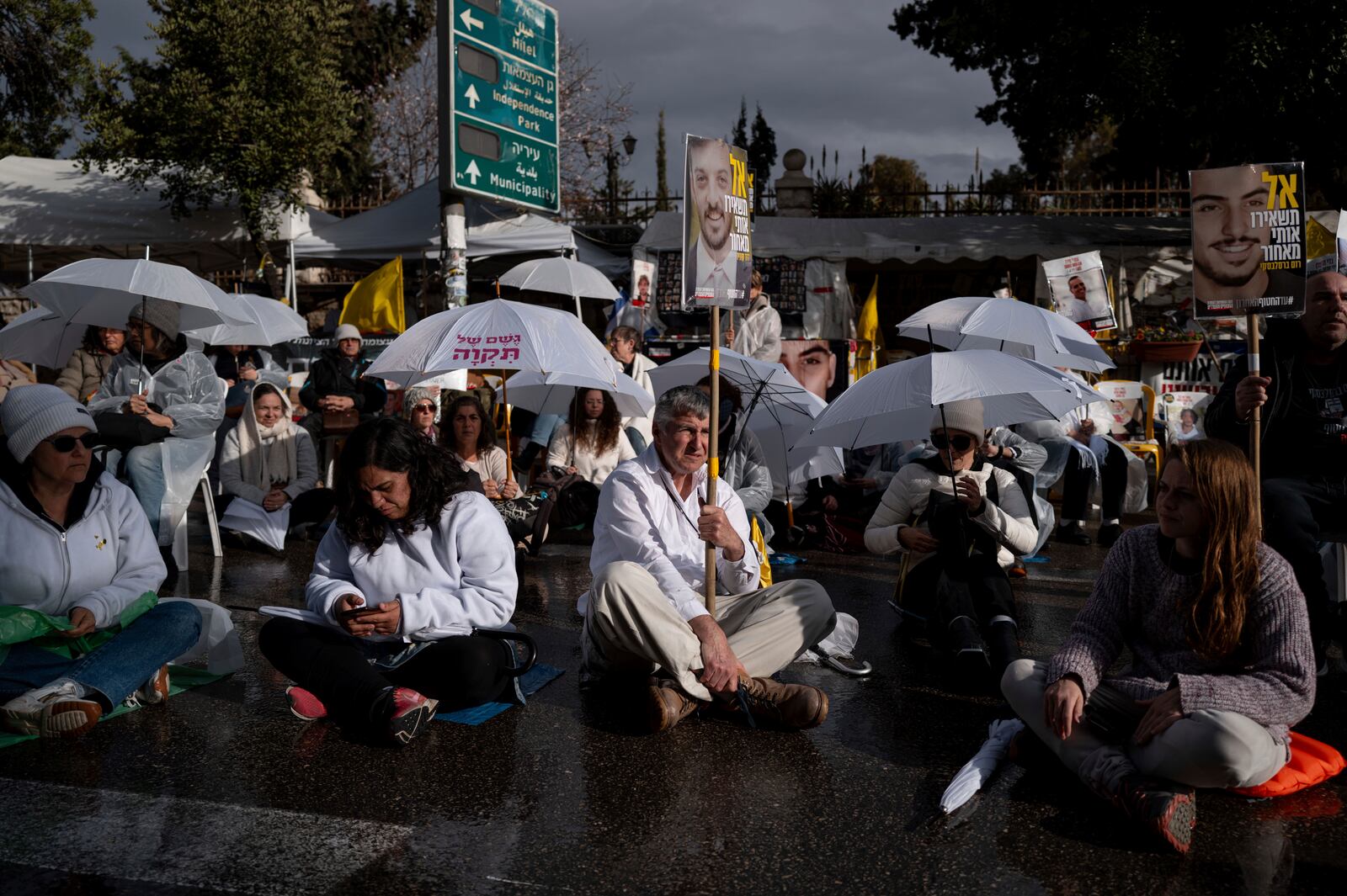 Activists sit on a road with white umbrellas during a protest calling for the release of hostages held in the Gaza Strip, outside the prime minister's house in Jerusalem, Wednesday, Feb. 12, 2025. (AP Photo/Ohad Zwigenberg)