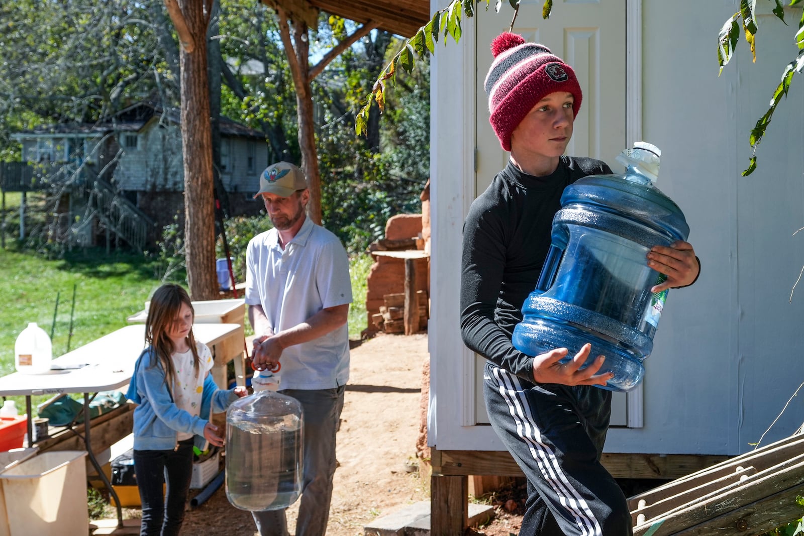 McCullough Hager, 12, carries one of the jugs of purified water that his father, Jessan Hager and sister, Jessa, 9, background, tapped from a community well located on an urban farm that belongs to Bountiful Cities, a nonprofit organization Monday, Oct. 14, 2024, in Asheville, N.C. (AP Photo/Kathy Kmonicek)