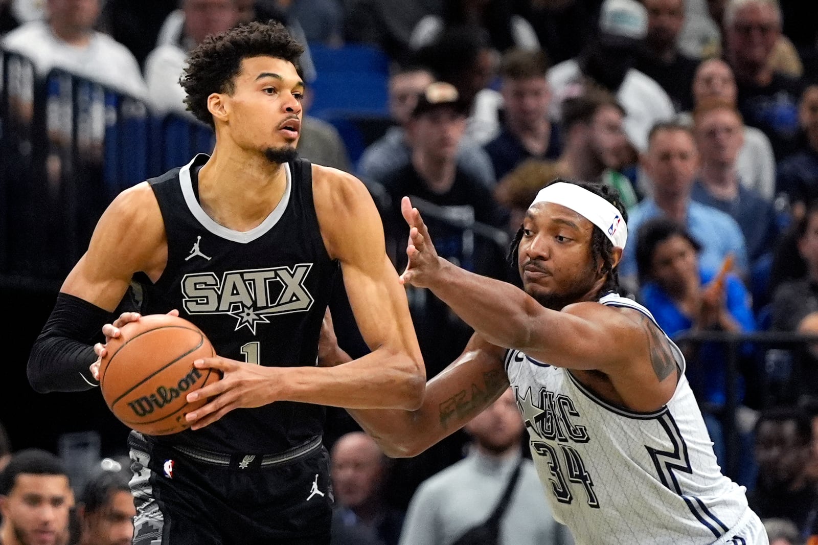 San Antonio Spurs center Victor Wembanyama, left, passes the ball around Orlando Magic center Wendell Carter Jr. (34) during the first half of an NBA basketball game Saturday, Feb. 8, 2025, in Orlando, Fla. (AP Photo/John Raoux)