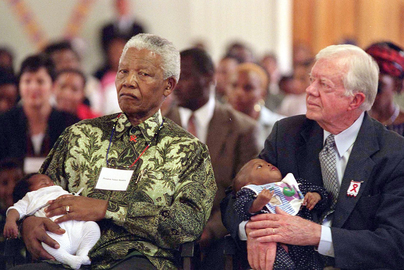 FILE - Former South African President Nelson Mandela, left, and former U.S. President Jimmy Carter, right, hold HIV-positive babies at the Zola Clinic in Soweto, March 7, 2002. (AP Photo/Nonthemba Kwela, File)