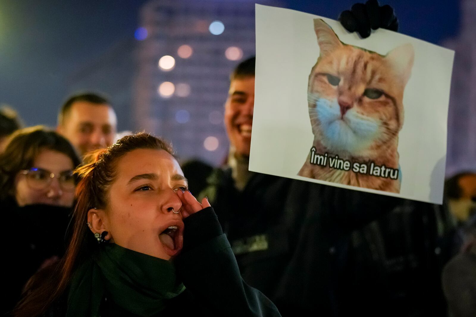 A woman shouts next to a banner depicting a grumpy cat with a text that reads "I feel like barking" in Bucharest, Romania, Wednesday, Nov. 27, 2024 during a protest against Calin Georgescu, the independent candidate for Romanian presidency who won the first round of elections making it to the Dec. 8, runoff. (AP Photo/Vadim Ghirda)