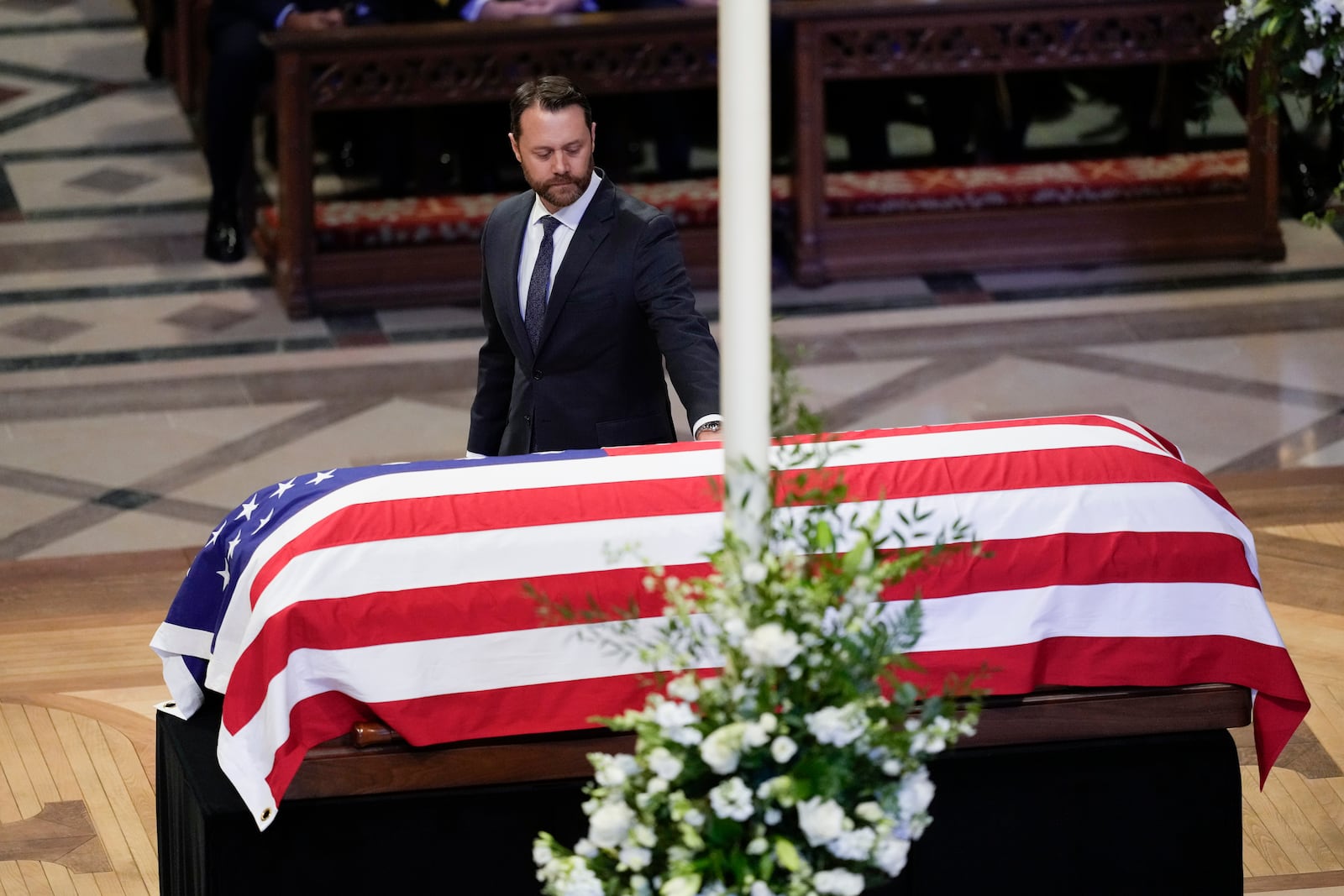 Grandson Jason Carter, walks by and touches the flag-draped casket of former President Jimmy Carter, after speaking a tribute at the state funeral for Carter at Washington National Cathedral, Thursday, Jan. 9, 2025, in Washington. (AP Photo/Ben Curtis)