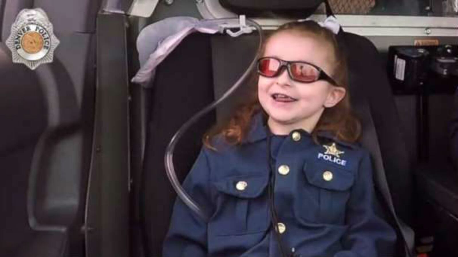 Olivia Gant grins while riding with a Denver police officer in a still from video shot in April 2017, about four months before the 7-year-old died. Her mother, Kelly Turner, is accused of lying about the girl's health for years before killing her.