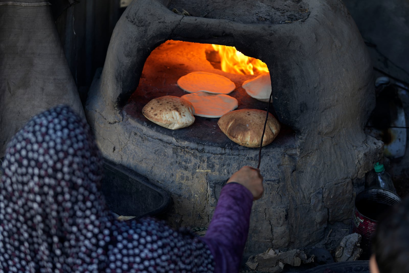 A Palestinian woman bakes bread in a clay oven amid dire food shortages in Deir al-Balah, Gaza Strip, Monday, Dec. 2, 2024. (AP Photo/Abdel Kareem Hana)