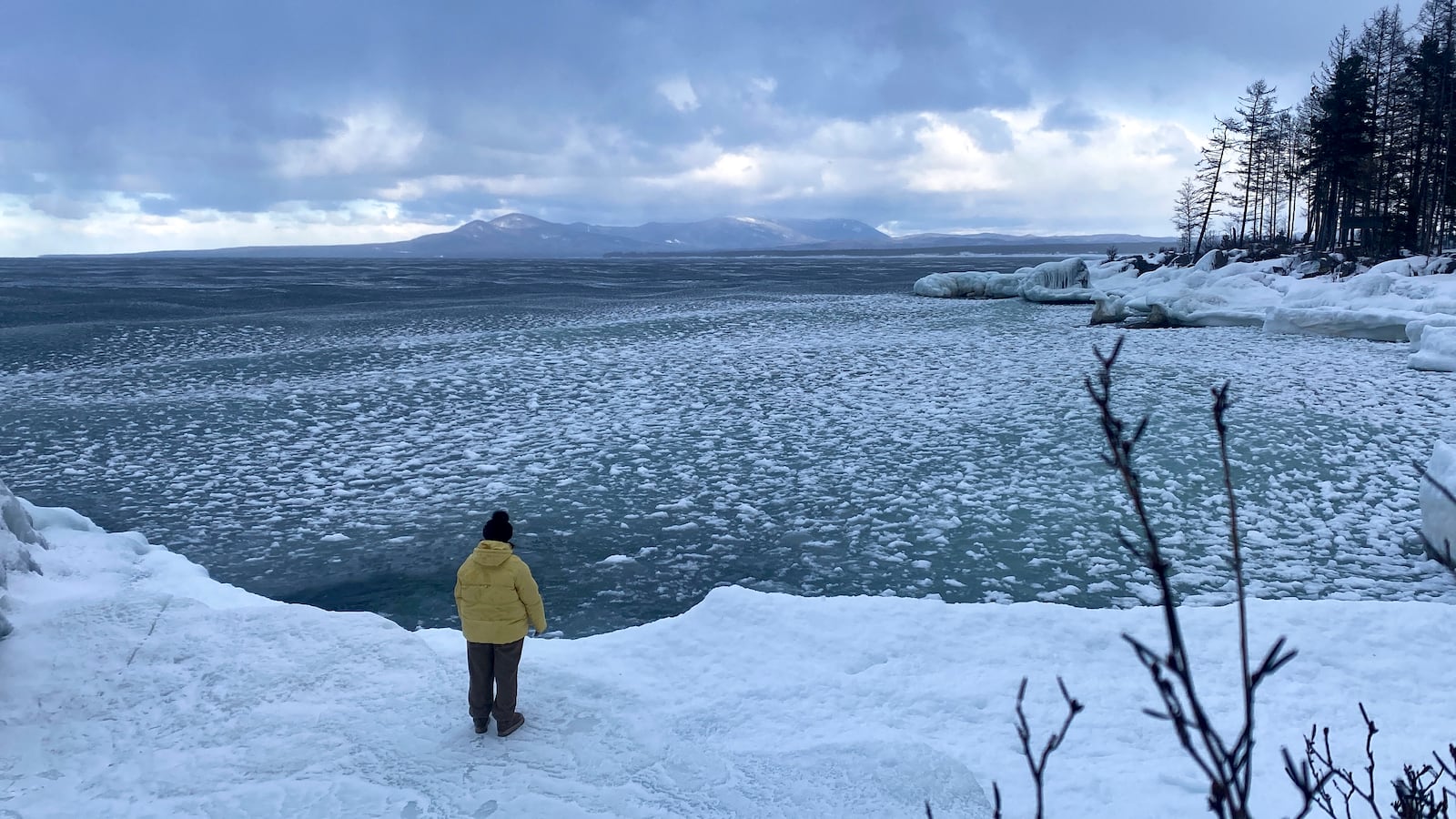 A tourist stands on the shore of Lake Baikal, which is typically covered in thick ice, near the village of Turka, Russia, on Wednesday, Jan. 1, 2025. (AP Photo)