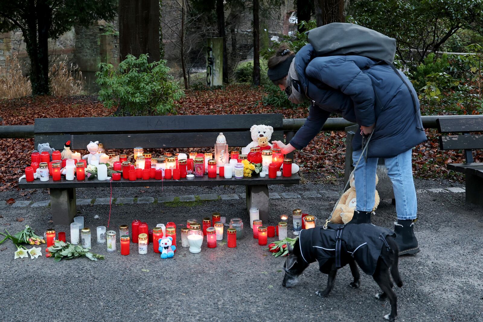 A woman places a mourning candle on a bench next to flowers and cuddly toys in Aschaffenburg, Germany, Thursday, Jan. 23, 2025 following the fatal attack in a park. (Daniel Loeb/dpa via AP)