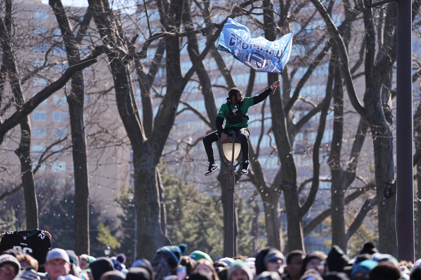 A fan waves a flag from atop a lamp post during the Philadelphia Eagles' NFL football Super Bowl 59 parade and celebration, Friday, Feb. 14, 2025, in Philadelphia. (AP Photo/Matt Rourke)