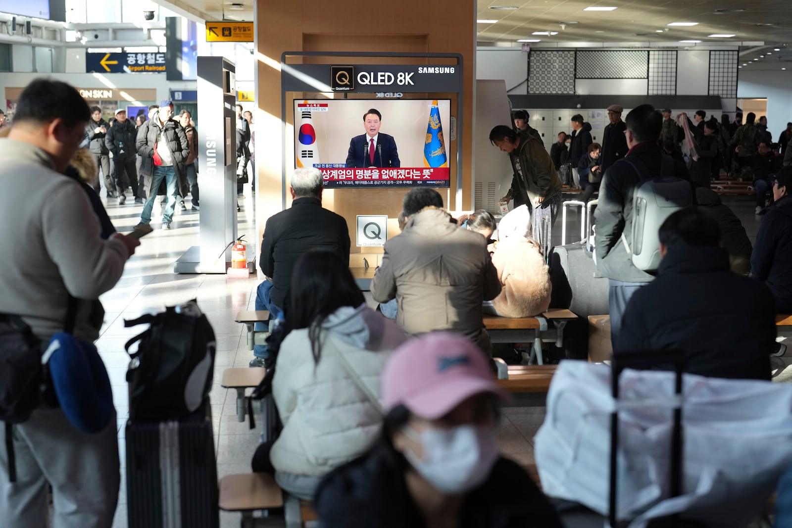 People watch a TV screen showing the live broadcast of South Korean President Yoon Suk Yeol's announcement at the Seoul Railway Station in Seoul, South Korea, Thursday, Dec. 12, 2024. (AP Photo/Lee Jin-man)