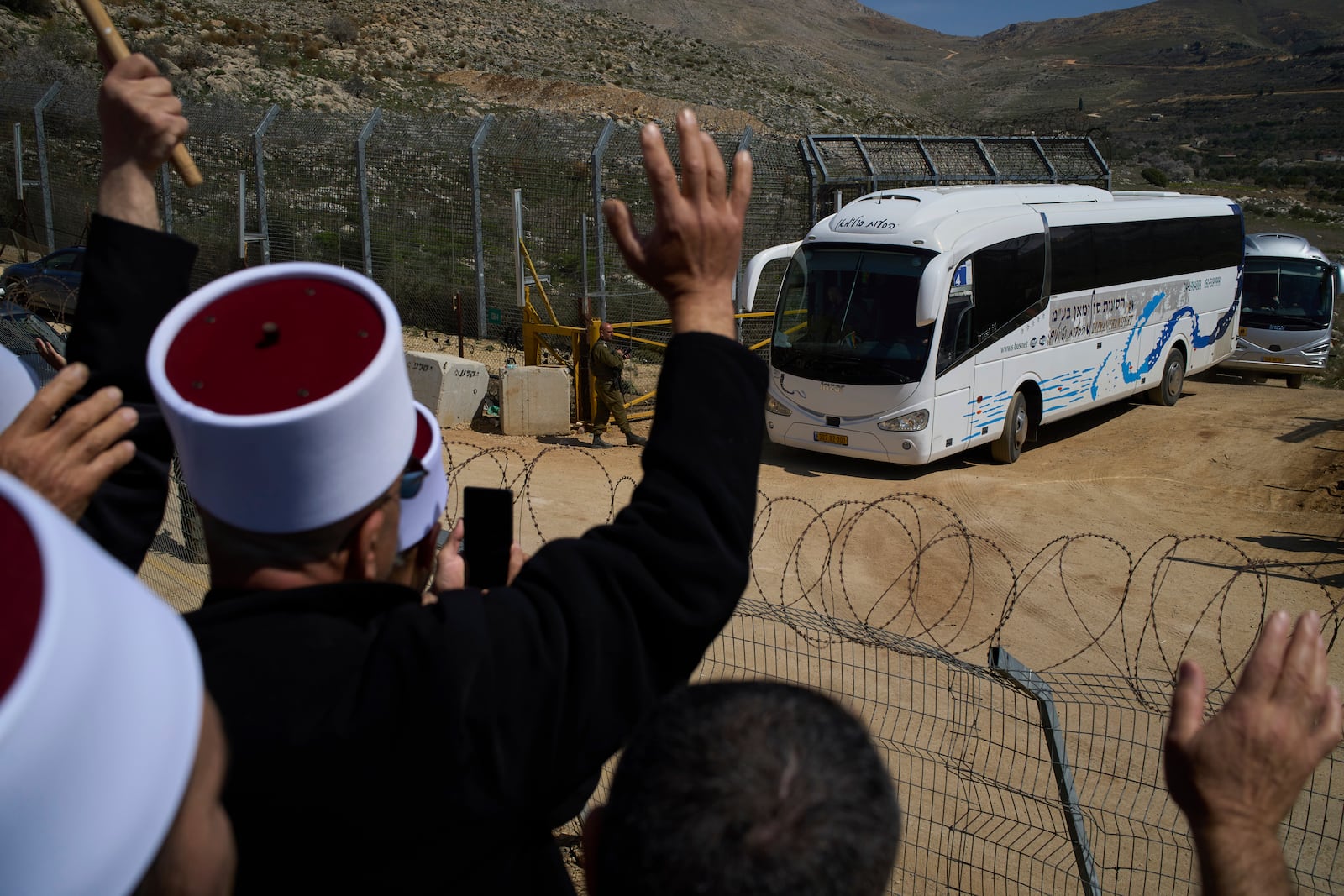 Buses carrying members of the Syrian Druze community are welcomed by Druze clerics at the border with Syria, as they enter into the village of Majdal Shams, in the Israeli-controlled Golan Heights, Friday, March 14, 2025. (AP Photo/Leo Correa)