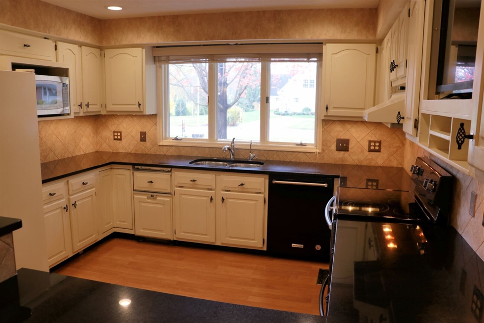 Three walls have white cabinetry and granite counters. Triple windows are above the double sink. A planning station has a media nook above and room for a coffee station. An elevated peninsula counter offers breakfast bar seating.