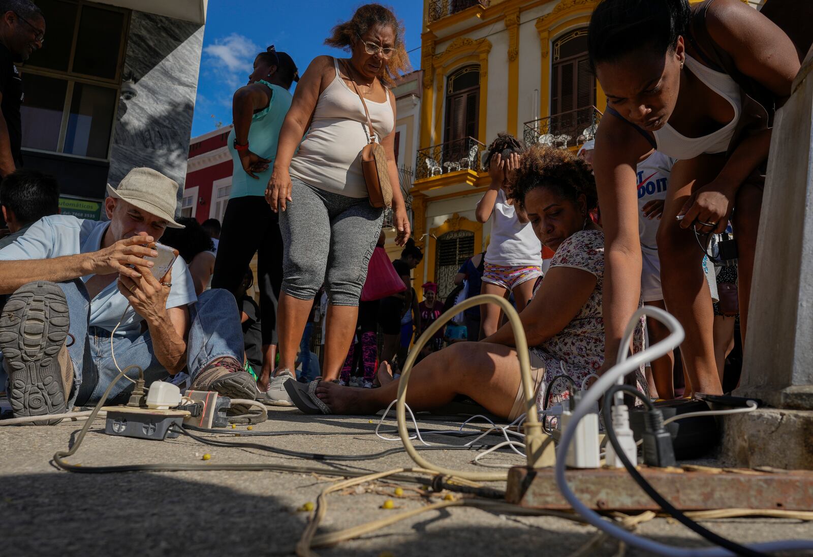 Residents charge their electronic devices on a street during a general blackout in Havana, Saturday, March 15, 2025. (AP Photo/Ramon Espinosa)