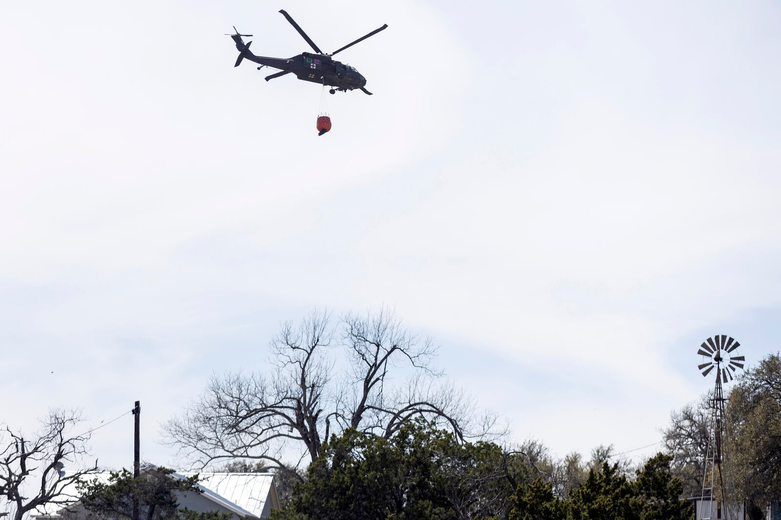 A helicopter carries a water tank as crews fight the Crabapple Fire near Fredericksburg, Texas, Monday, March 17, 2025. (Josie Norris/The San Antonio Express-News via AP)