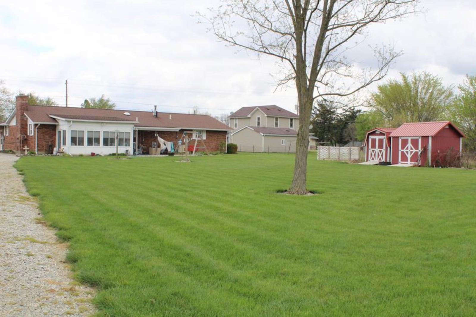 The rear of the home has a sunroom connected to a covered concrete patio. The yard is fully fenced and has two yard barns, a horse barn and pasture.