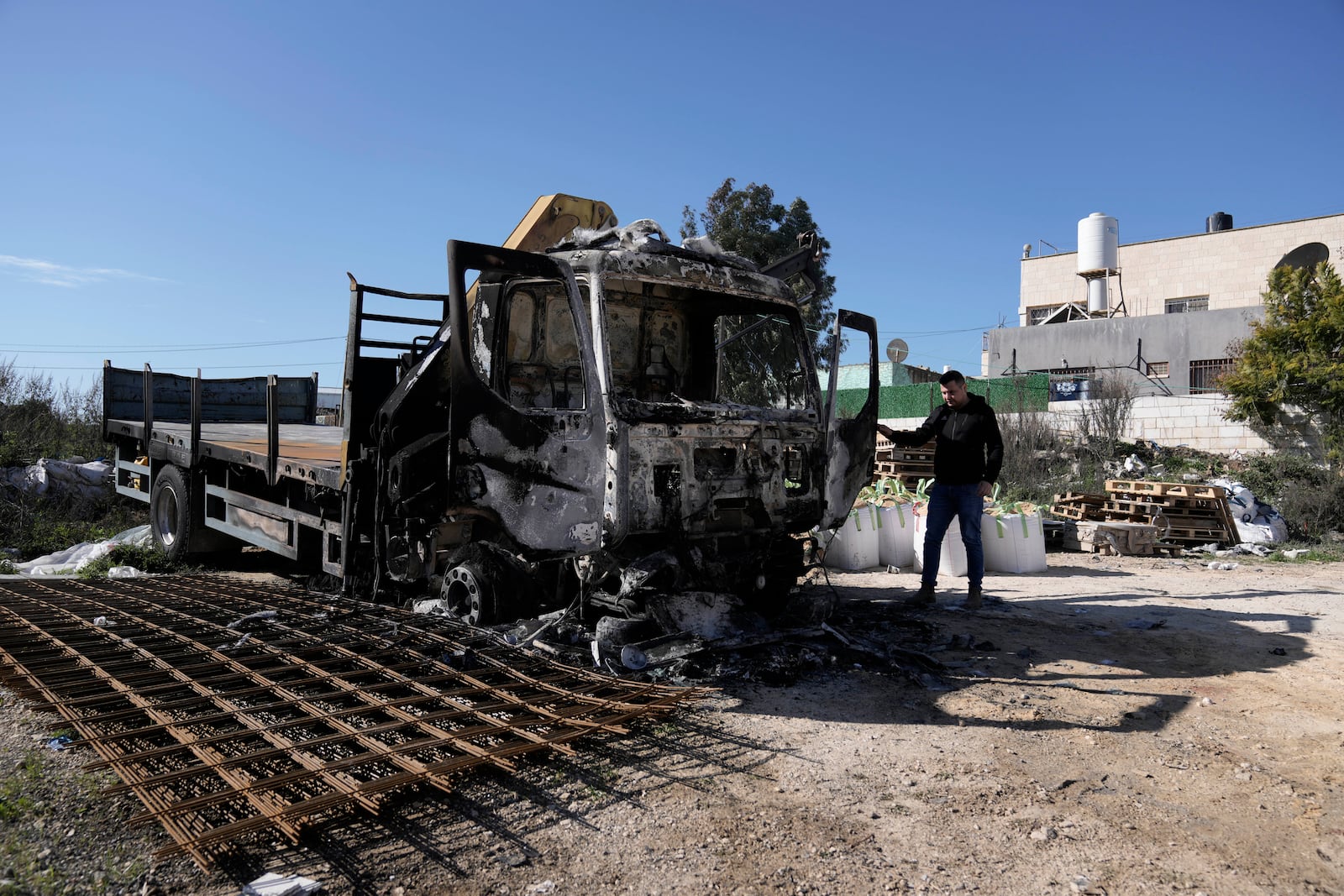 A Palestinian stands beside a trick that was torched in an attack by Israeli settlers in the West Bank village of Jinsafut, Tuesday, Jan. 21, 2025. (AP Photo/Majdi Mohammed)