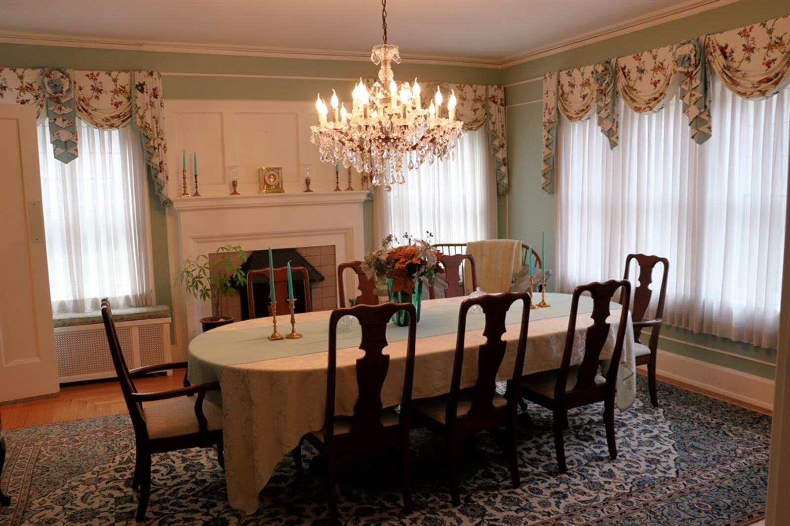 The dining room walls have picture-frame wainscoting and crown molding. A fireplace has a bold mantel and marble surround. A swinging door opens into a butler’s pantry, which has been updated to include bottle and glass racks, cabinetry, granite counters for a coffee station and a mini-refrigerator.