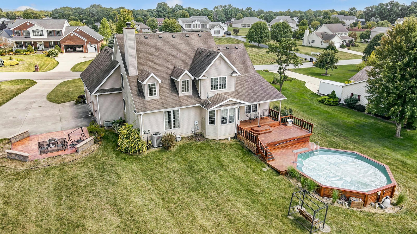 The rear of the home has a covered wood deck that steps down to an above ground pool with wood surround. There is also a stamped firepit area attached to the driveway.