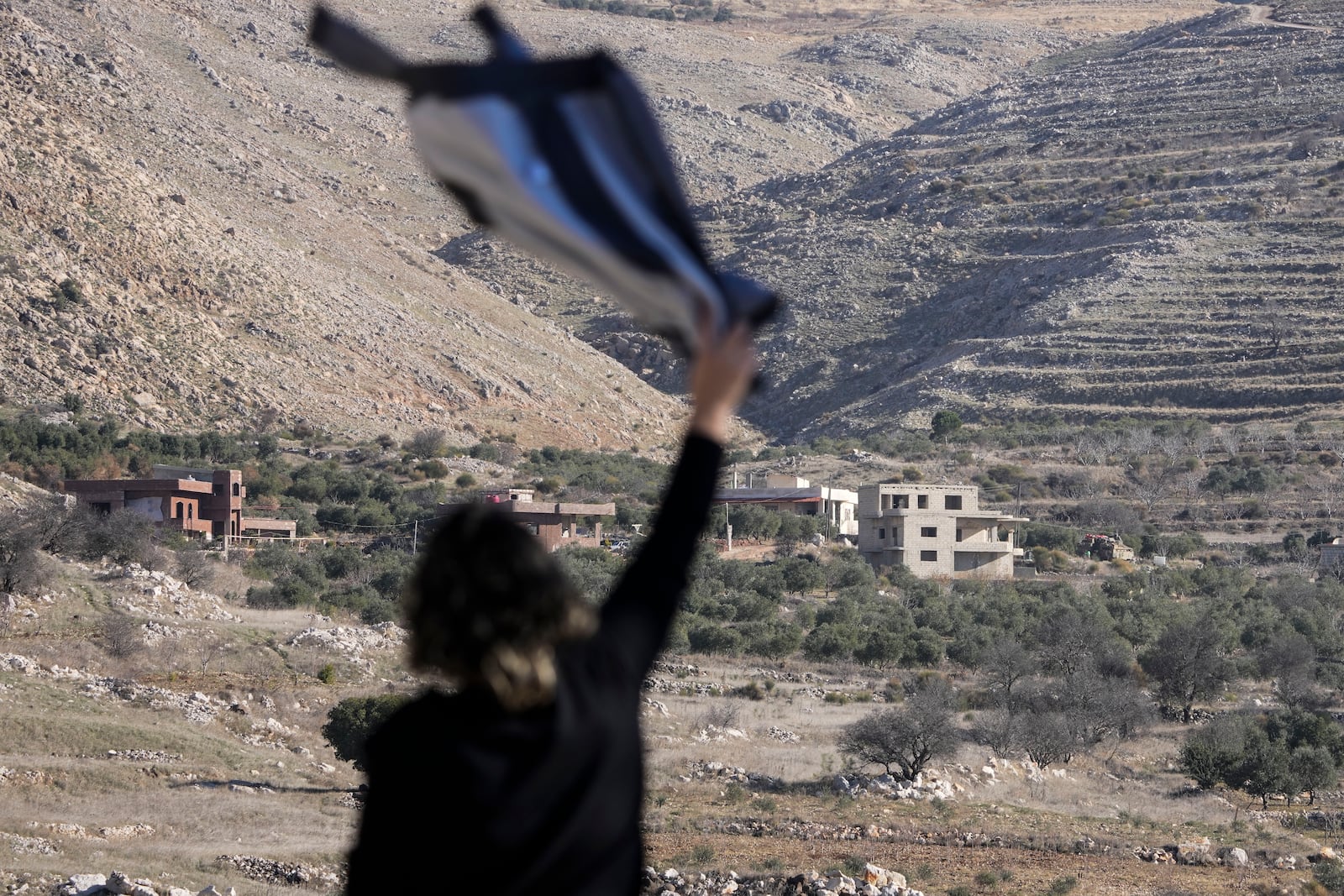 A woman waves a shirt to her relative who lives inside the buffer zone near the so-called Alpha Line that separates the Israeli-controlled Golan Heights from Syria, in the town of Majdal Shams, Tuesday, Dec. 17, 2024. (AP Photo/Matias Delacroix)