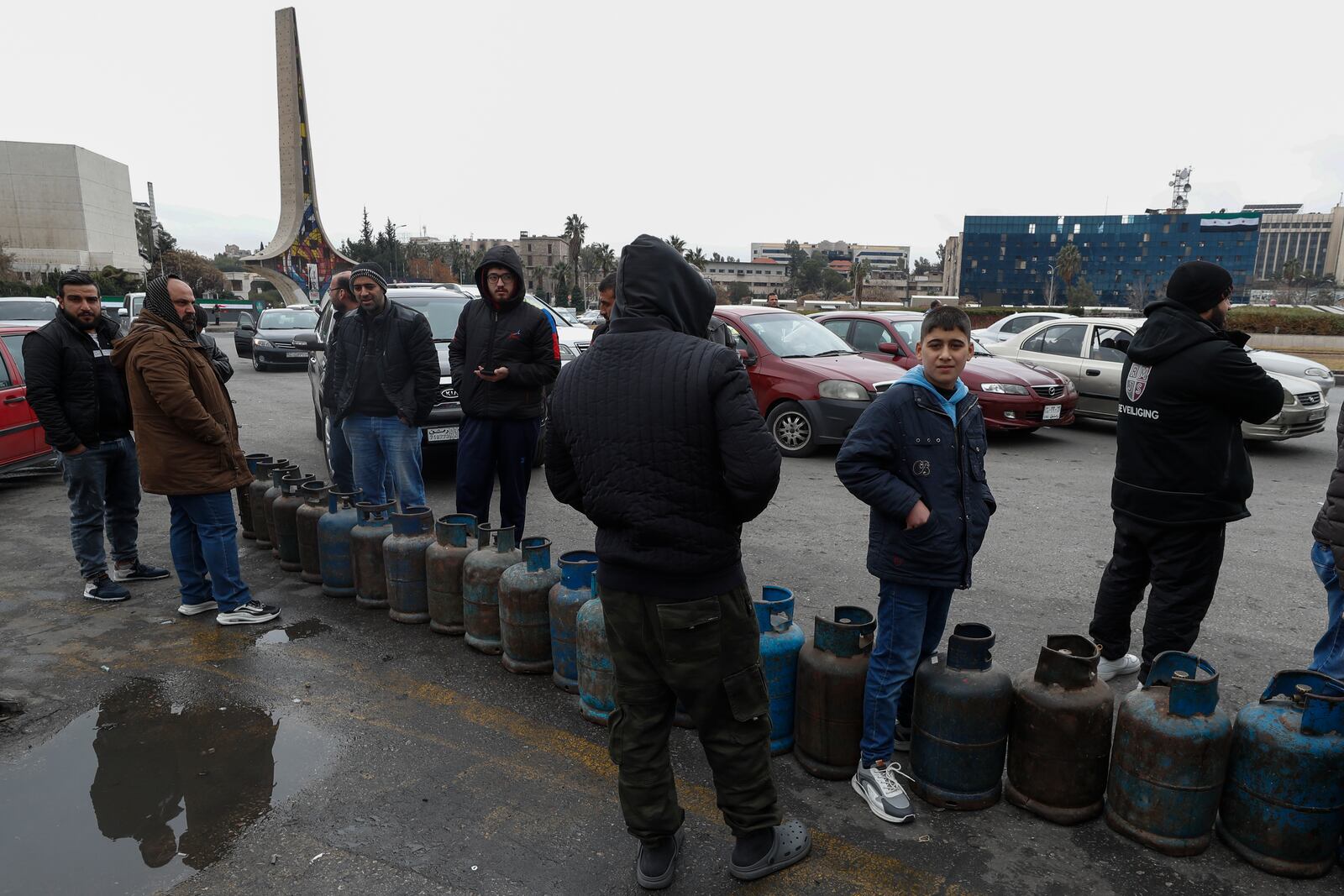 People stand next to cylinders as they wait in line to buy gas on a street at the Umayyad Square in Damascus, Syria, Saturday, Dec. 28, 2024. (AP Photo/Omar Sanadiki)