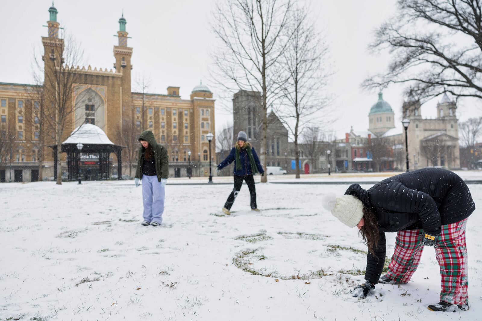 Lauren Phillips bends down to draw a head for her snow angel while her friends Ellie Sims and Amilia Muller look at their snow angels in Monroe Park, Wednesday, Feb. 19, 2025, in Richmond, Va. (Margo Wagner/Richmond Times-Dispatch via AP)