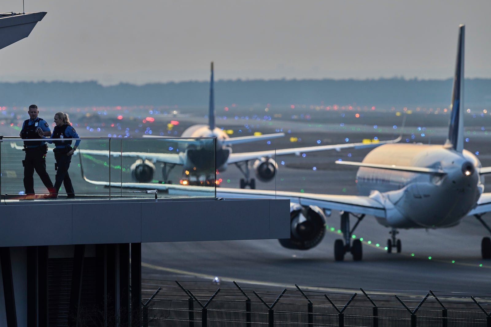 Police officers watch aircrafts take their parking positions at the airport in Frankfurt, Germany, Sunday, March 9, 2025, the evening before a warning strike of all major German airports. (AP Photo/Michael Probst)