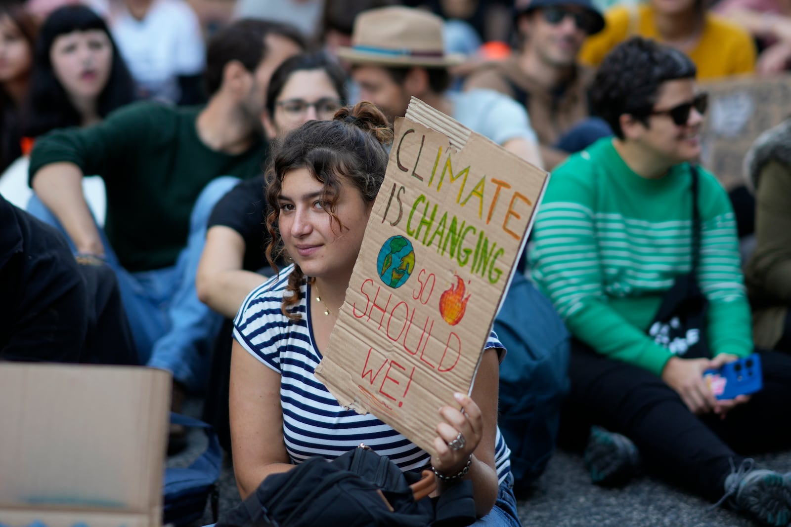 A demonstrator sitting on the ground holds a poster during a climate protest in Lisbon, to coincide with the closing of the COP29 Climate Summit Saturday, Nov. 23, 2024. (AP Photo/Armando Franca)