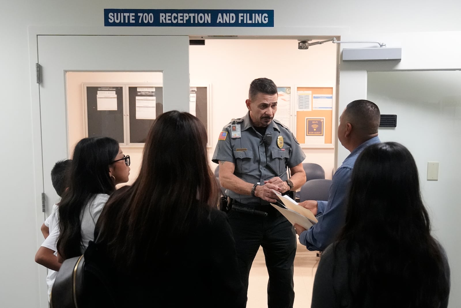 FILE - An officer listens to a question as he directs people to a courtroom, Jan. 10, 2024, in an immigration court in Miami. (AP Photo/Wilfredo Lee, File)