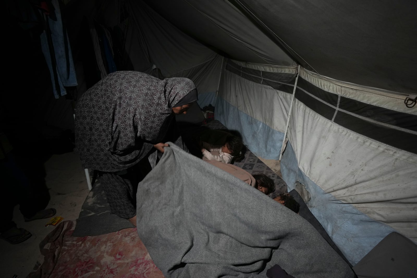 Shireen Daifallah, who was displaced from northern Gaza, checks one of her children in their tent at a camp for displaced people in Deir al-Balah. Gaza Strip, Saturday, Nov. 30, 2024. (AP Photo/Abdel Kareem Hana)