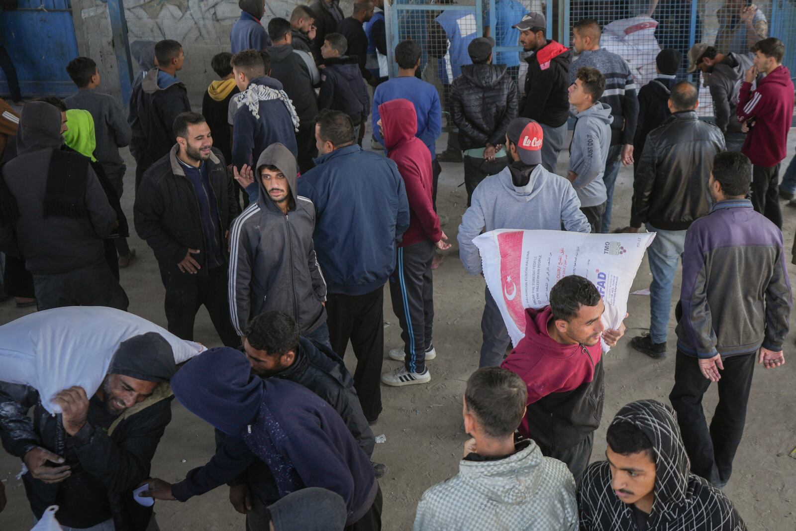 Palestinians carry sacks of donated flour at a UNRWA distribution center in the Nuseirat refugee camp, Gaza Strip, Tuesday Dec. 3, 2024.(AP Photo/Abdel Kareem Hana)