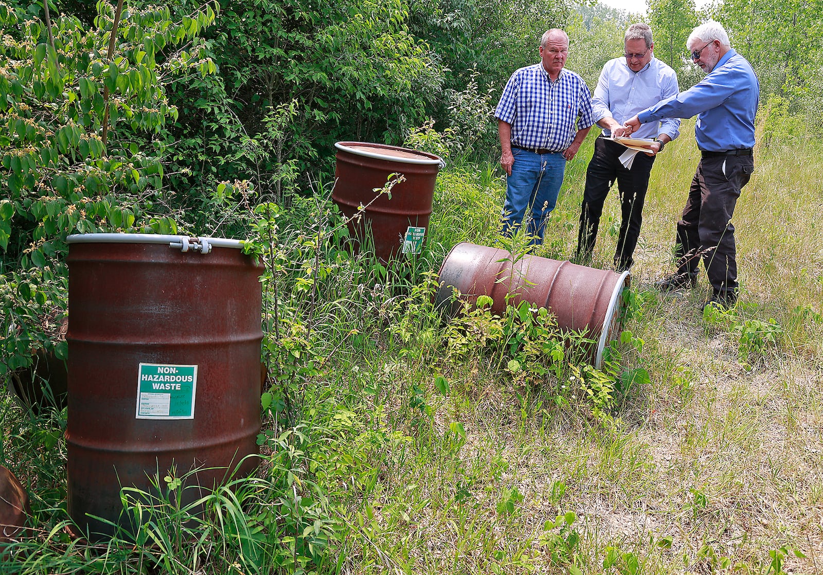 Bob Rule, from the "potential responsible party" group, center, along with German Township Trustee Rodney Kaffenbarger, left, and Larry Ricketts look over a map for the Tremont City Barrel Fill Wednesday, June 7, 2023. The barrels, at left, were empty but used during testing. BILL LACKEY/STAFF