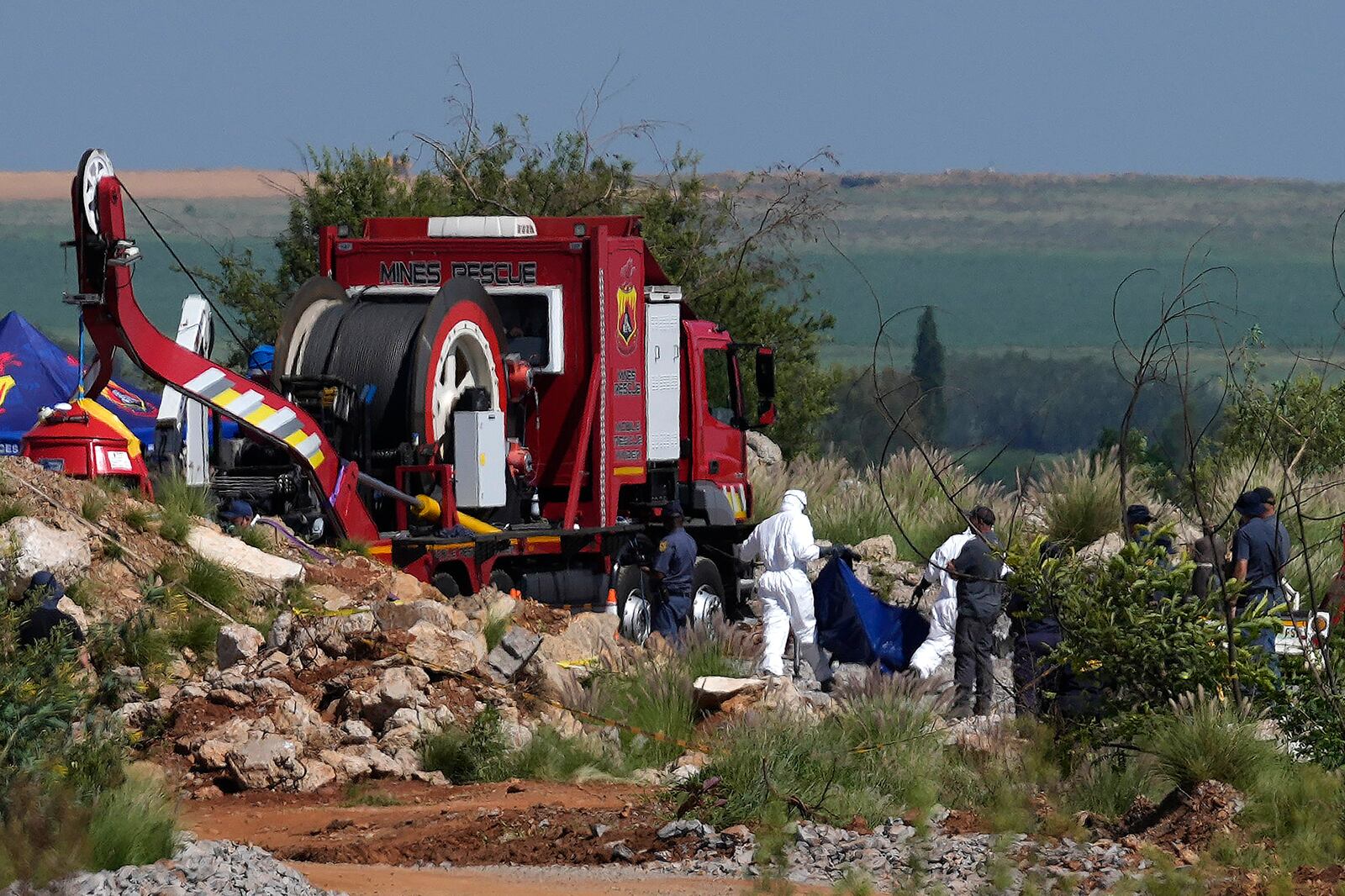 Forensic service workers carry remains in blue body bags during a rescue operation to rescue miners from below ground in an abandoned gold mine in Stilfontein, South Africa, Tuesday, Jan. 14, 2025. (AP Photo/Themba Hadebe)