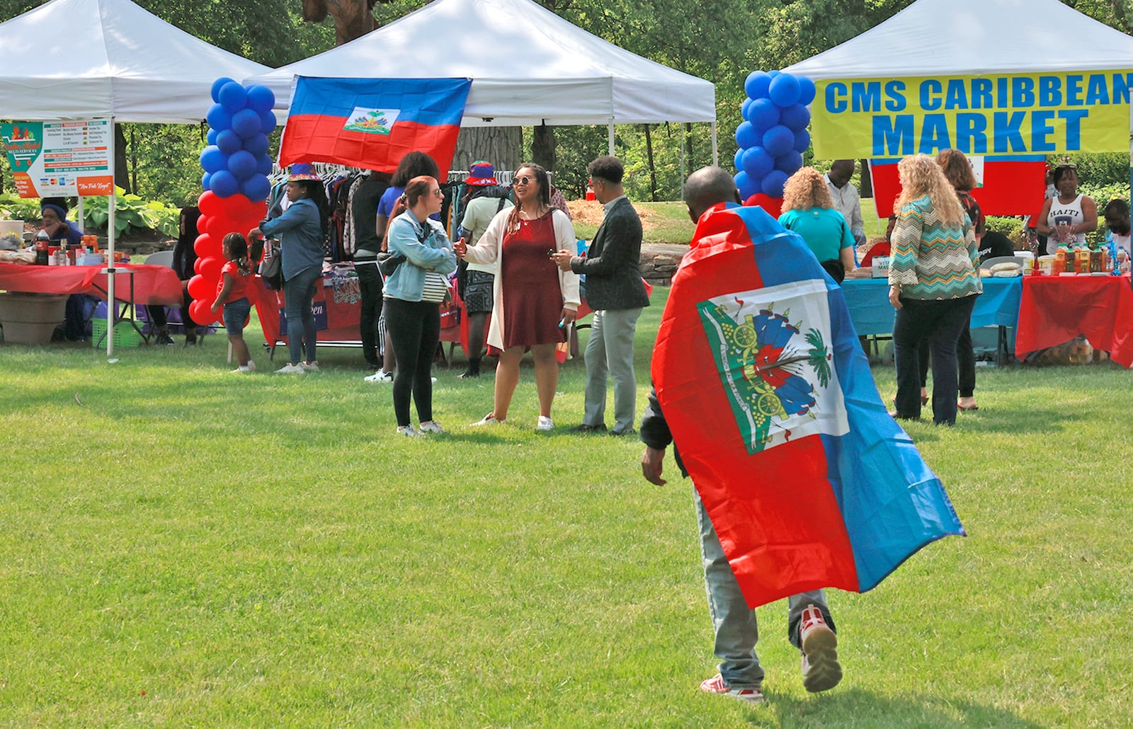 A man wears a Haitian flag as a cape Thursday, May 18, 2023 as he walks through the Haitian Flag Day Festival in Veterans Park. BILL LACKEY/STAFF