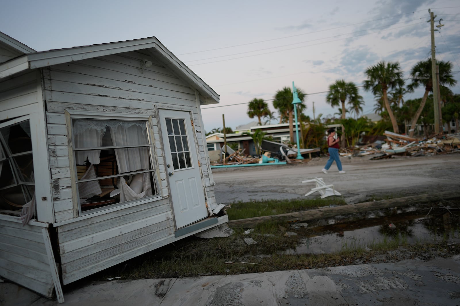 A woman, right, walks past a home that was swept partially into the road during the passage of Hurricane Milton, on Manasota Key, Fla., Saturday, Oct. 12, 2024. (AP Photo/Rebecca Blackwell)