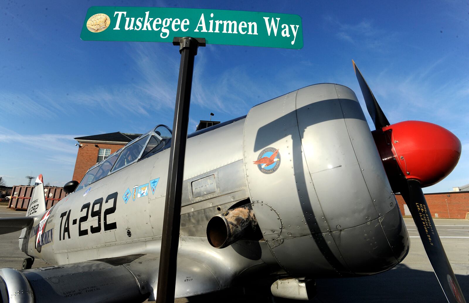 FILE - The Tuskegee Airmen Way street sign is briefly displayed in front of a 1943 North American T6 Texan aircraft used to train pilots during WWII, at the Selfridge Air National Guard Base, in Harrison Township, Mich., Feb. 27, 2018. The street-renaming event honored the heritage of the Tuskegee Airmen at Selfridge. (Todd McInturf/Detroit News via AP, File)