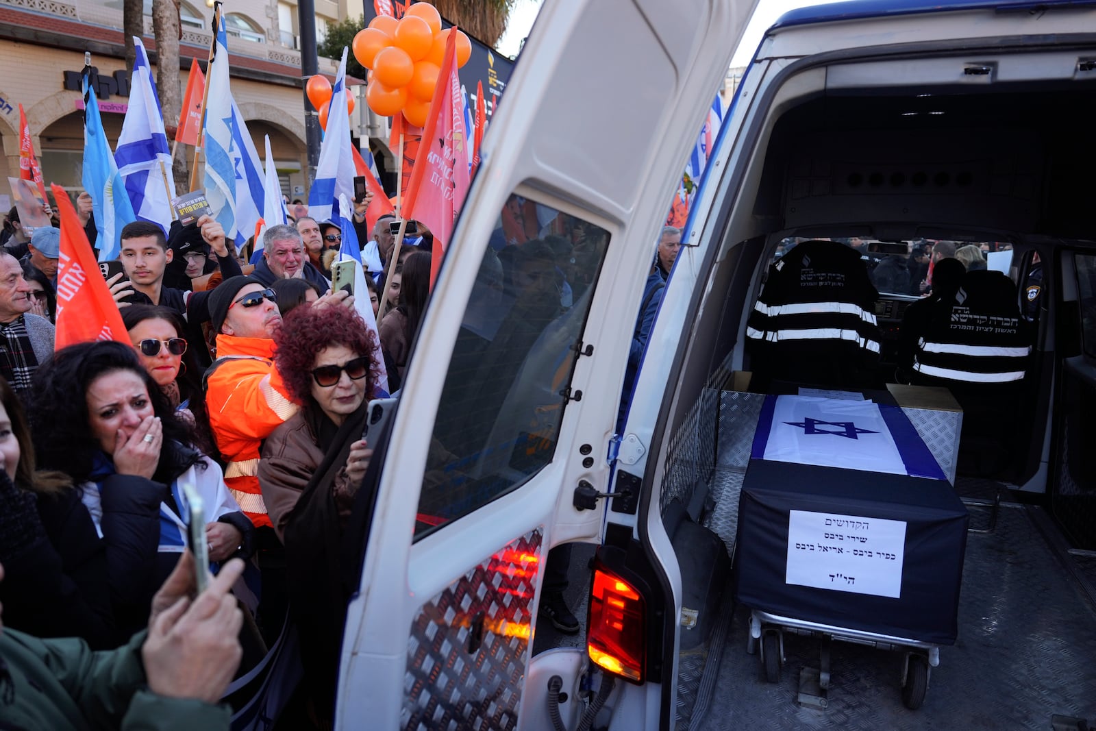 Mourners gather around the car carrying the coffins of slain hostages Shiri Bibas and her two children, Ariel and Kfir, during their funeral procession in Rishon Lezion, Israel, Wednesday, Feb. 26, 2025. The mother and her two children were abducted by Hamas on Oct. 7, 2023, and their remains were returned from Gaza to Israel last week as part of a ceasefire agreement with Hamas. (AP Photo/Ariel Schalit)