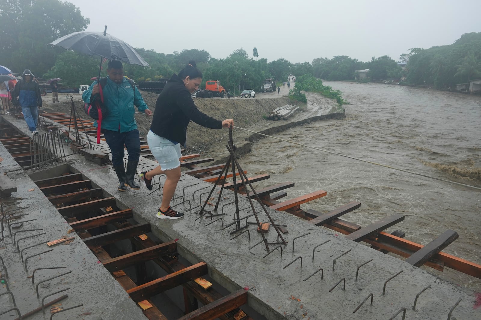 Residents cross a bridge under construction amid rain showers brought on by Tropical Storm Sara, on the outskirts of San Pedro Sula, Honduras, Saturday, Nov. 16, 2024. (AP Photo/Moises Castillo)