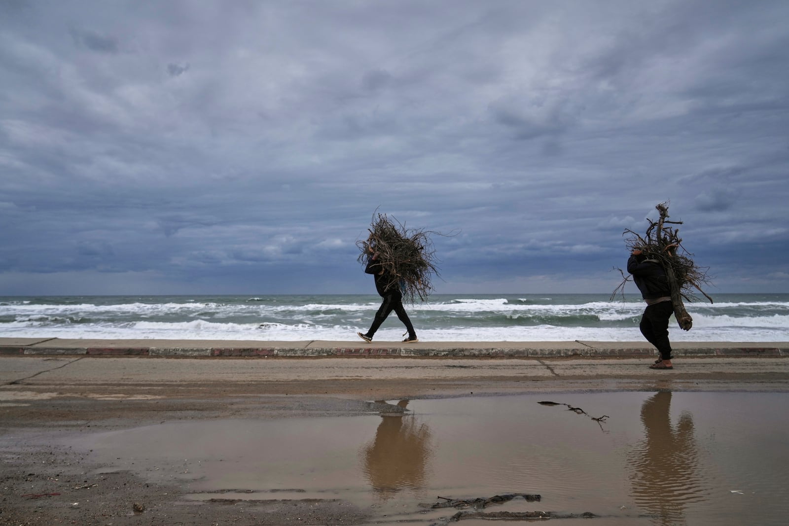 Palestinians carry bundles of wood as they walk along a beach road leaving northern Gaza during the renewed Israeli army offensive in the Gaza Strip, Friday March 21, 2025. (AP Photo/Abdel Kareem Hana)