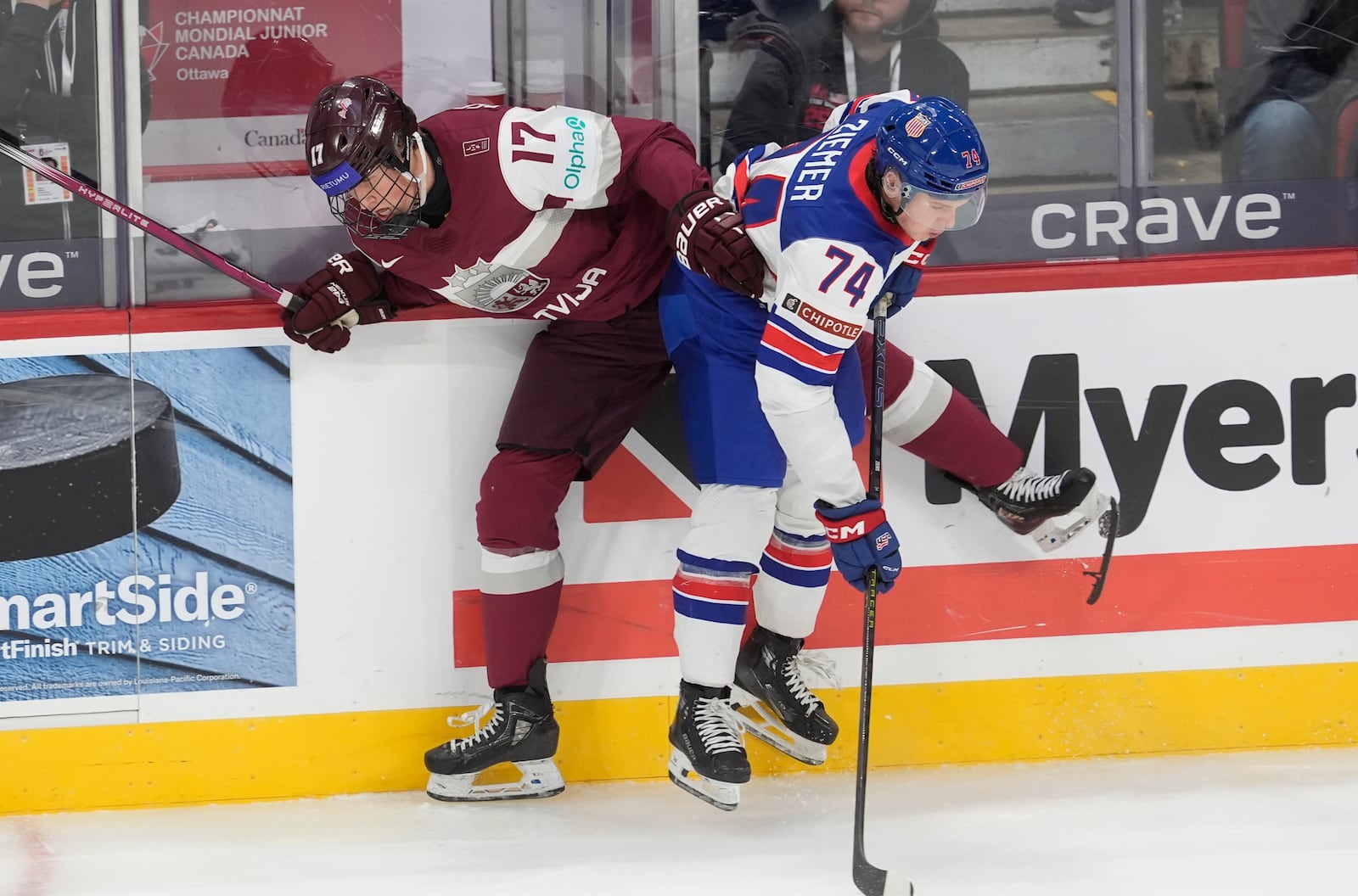 Latvia forward Rudolfs Berzkalns (17) loses a skate blade as he is checked by United States forward Brodie Ziemer (74) during the third period of a IIHF World Junior Hockey Championship tournament game, Saturday, Dec.28, 2024 in Ottawa, Ontario. (Adrian Wyld/The Canadian Press via AP)