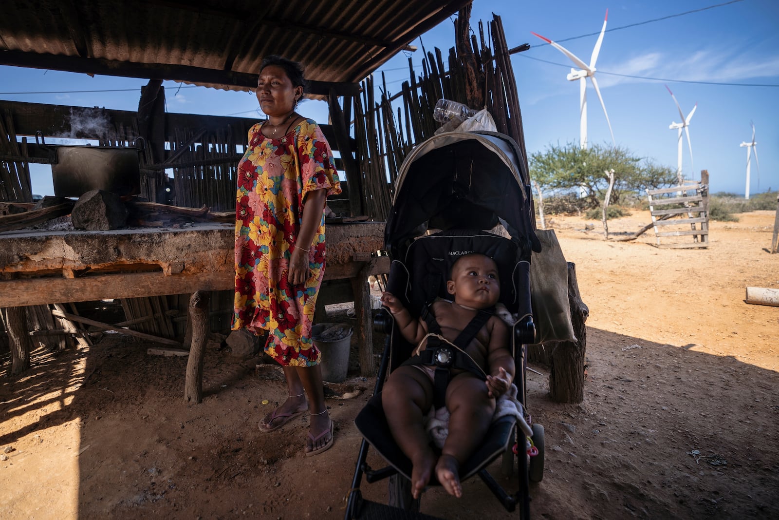 An Indigenous woman from the Wayuu community cooks near her baby as wind turbines operate in the distance on the outskirts of Cabo de la Vela, Colombia, Friday, Feb. 7, 2025. (AP Photo/Ivan Valencia)