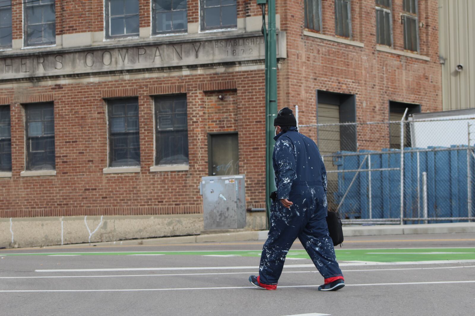 A worker in paint-splattered overalls walks along Wayne Avenue in downtown Dayton. CORNELIUS FROLIK / STAFF