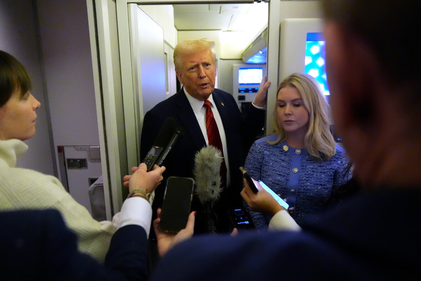 President Donald Trump speaks to reporters aboard Air Force One en route from Miami to Joint Base Andrews, Md., Monday, Jan. 27, 2025, as White House press secretary Karoline Leavitt listens. (AP Photo/Mark Schiefelbein)