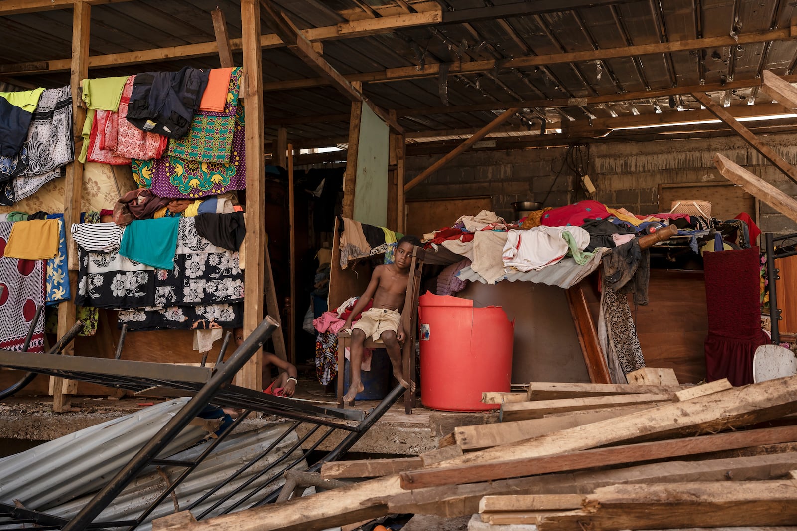 A boy sits in his destroyed home in the Kaweni slum on the outskirts of Mamoudzou in the French Indian Ocean island of Mayotte, Thursday, Dec. 19, 2024, after Cyclone Chido. (AP Photo/Adrienne Surprenant)