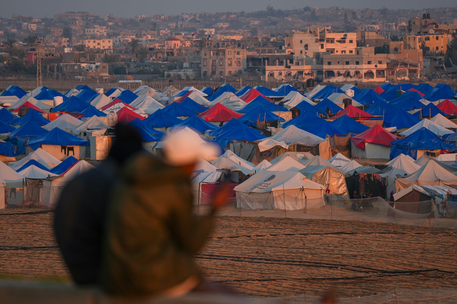 Two people sit at sunset overlooking a tent camp for displaced Palestinians in the outskirts in the central Gaza Strip town of Khan Younis Wednesday, Jan. 1, 2025. (AP Photo/Abdel Kareem Hana)