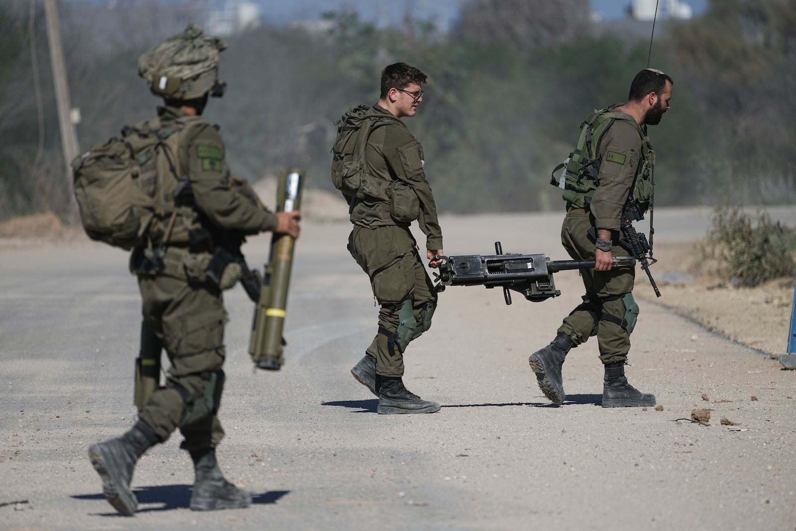 Israeli soldiers carry combat equipment as they return from the Gaza Strip at the Israeli-Gaza border, Saturday, Jan. 18, 2025. (AP Photo/Tsafrir Abayov)