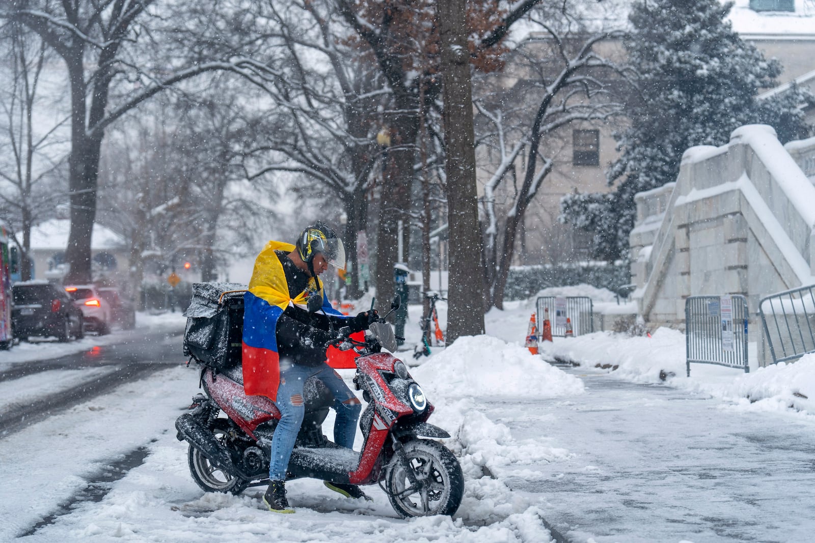 A man wearing a Venezuelan flag starts a moped as snow begins to fall again, Monday, Jan. 6, 2025, in Washington. (AP Photo/Jacquelyn Martin)