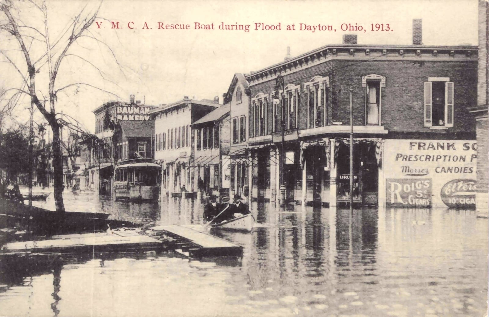 A YMCA rescue boat makes its way down Third Street in Dayton during the flood of 1913. A streetcar is stranded in the street behind it. “Looking west on Third St. This is the Green Line car that was caught in the flood. It was the next one out of Dayton after the one I caught and got through on,” is hand written on the back. DAYTON METRO LIBRARY