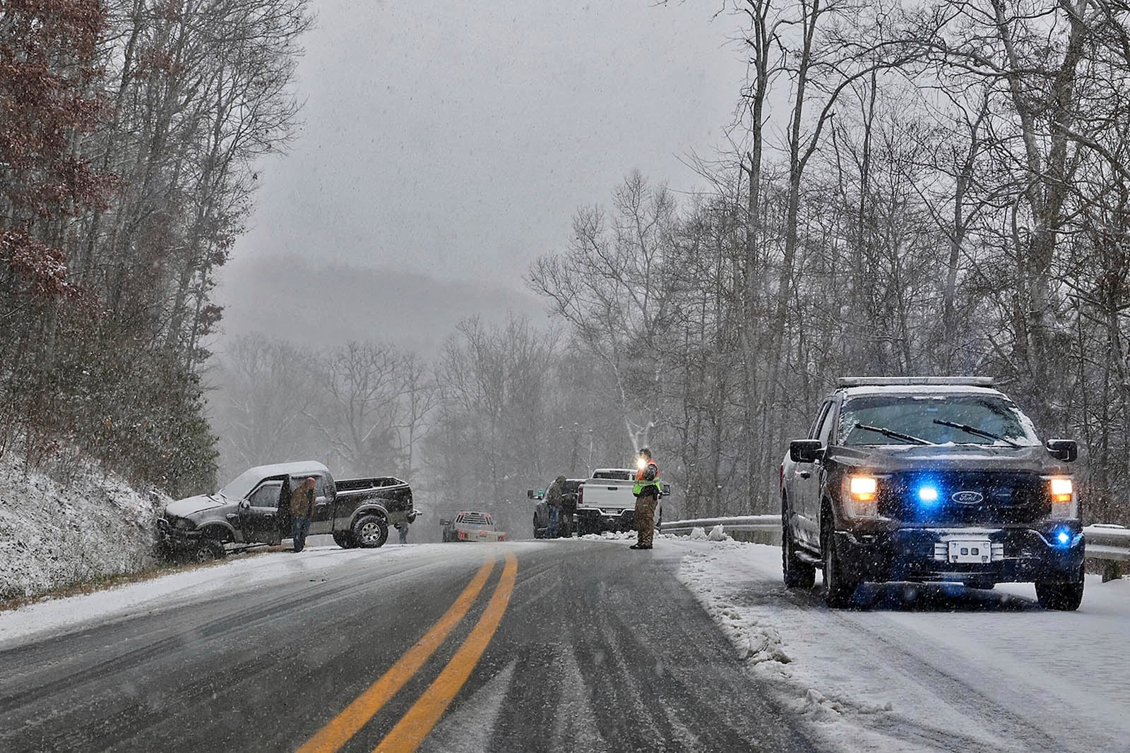 A driver, left, waits for his truck to be removed from an accident site after sliding into a hillside during snow showers, Thursday, Nov. 21, 2024, near Quinwood, W.Va. (Jenny Harnish/The Register-Herald via AP)