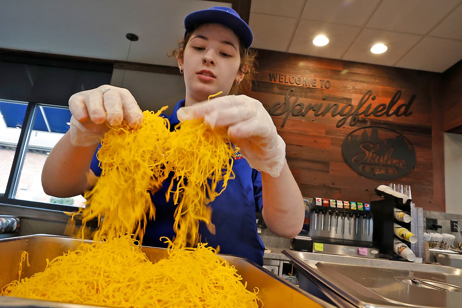 Brooklynn Knox, an employee at the new Skyline Chili in Springfield, fluffs the cheese before dividing it up into individual bags Wednesday, March 22, 2023. The employees and managers have been getting the new restaurant ready for it's grand opening on Thursday. BILL LACKEY/STAFF