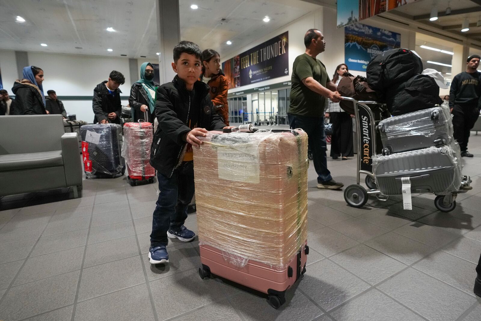 Mohammad Shabir Osmani, pushes one of his families suitcases out of the Sacramento International Airport, Tuesday, March 11, 2025. (AP Photo/Rich Pedroncelli)