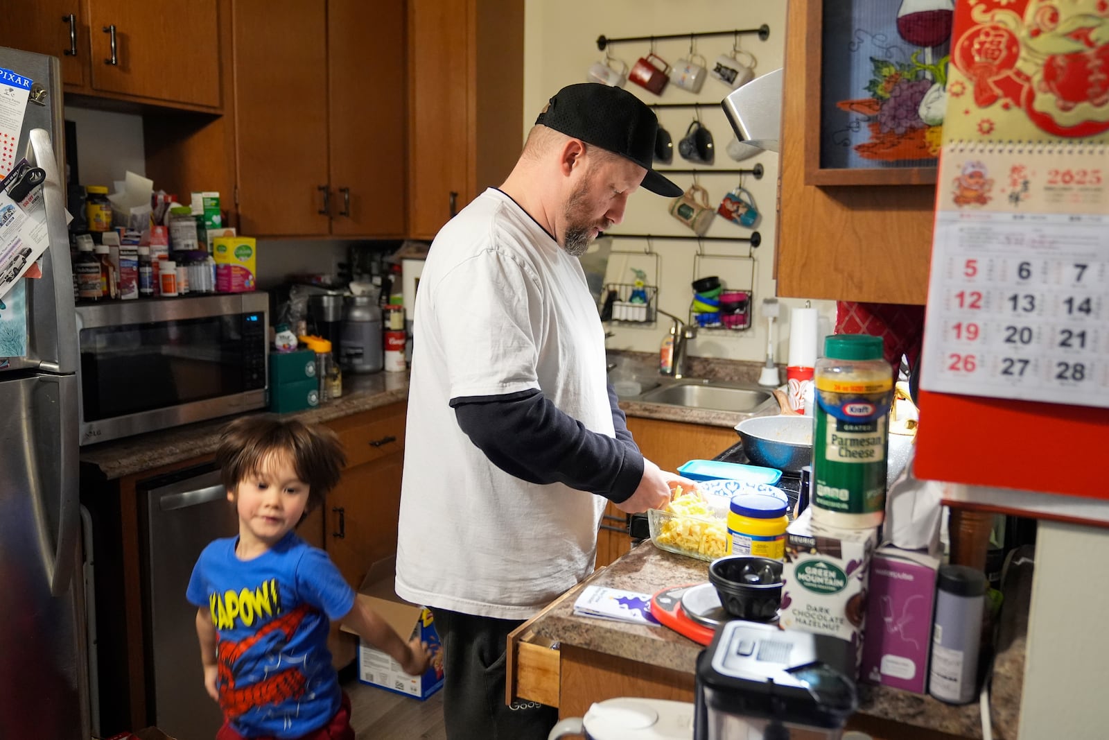 Steve Petersen, right, prepares dinner for his 4-year-old son, Jerrik, inside their apartment in Campbell, Calif., Wednesday, Jan. 15, 2025. (AP Photo/Godofredo A. Vásquez)