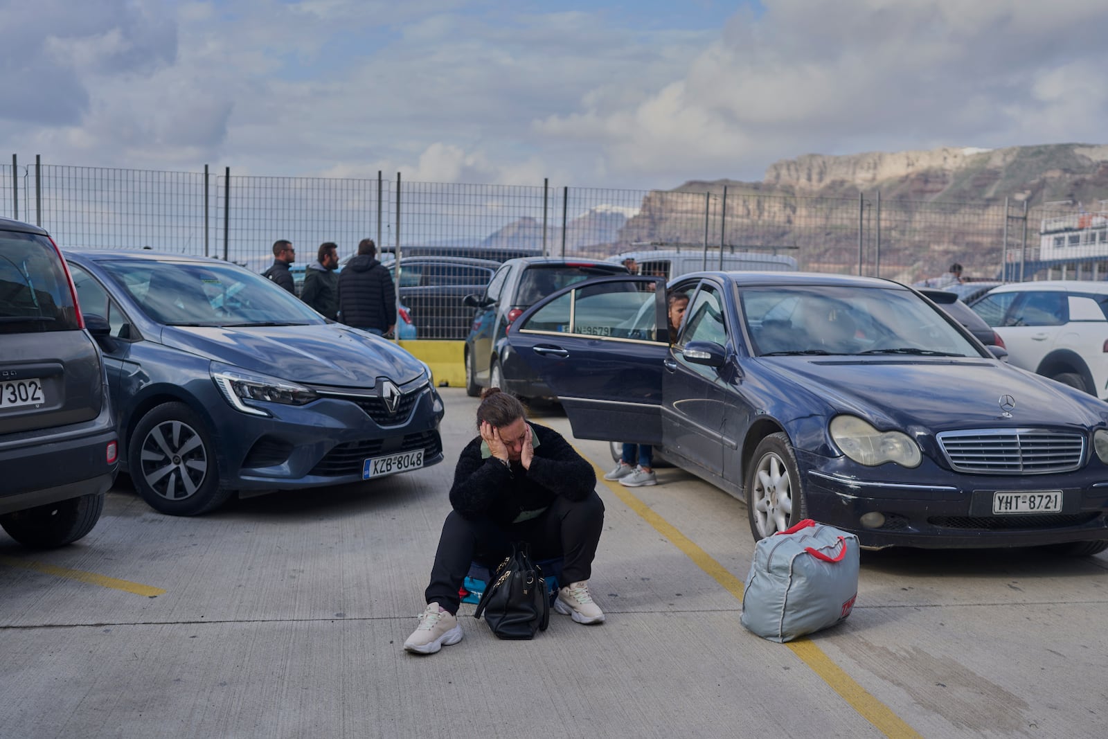 A passenger sits on the dock while waiting for a ferry bound for the Greek mainland, in the earthquake-struck island of Santorini, Greece, Tuesday, Feb. 4, 2025. (AP Photo/Petros Giannakouris)